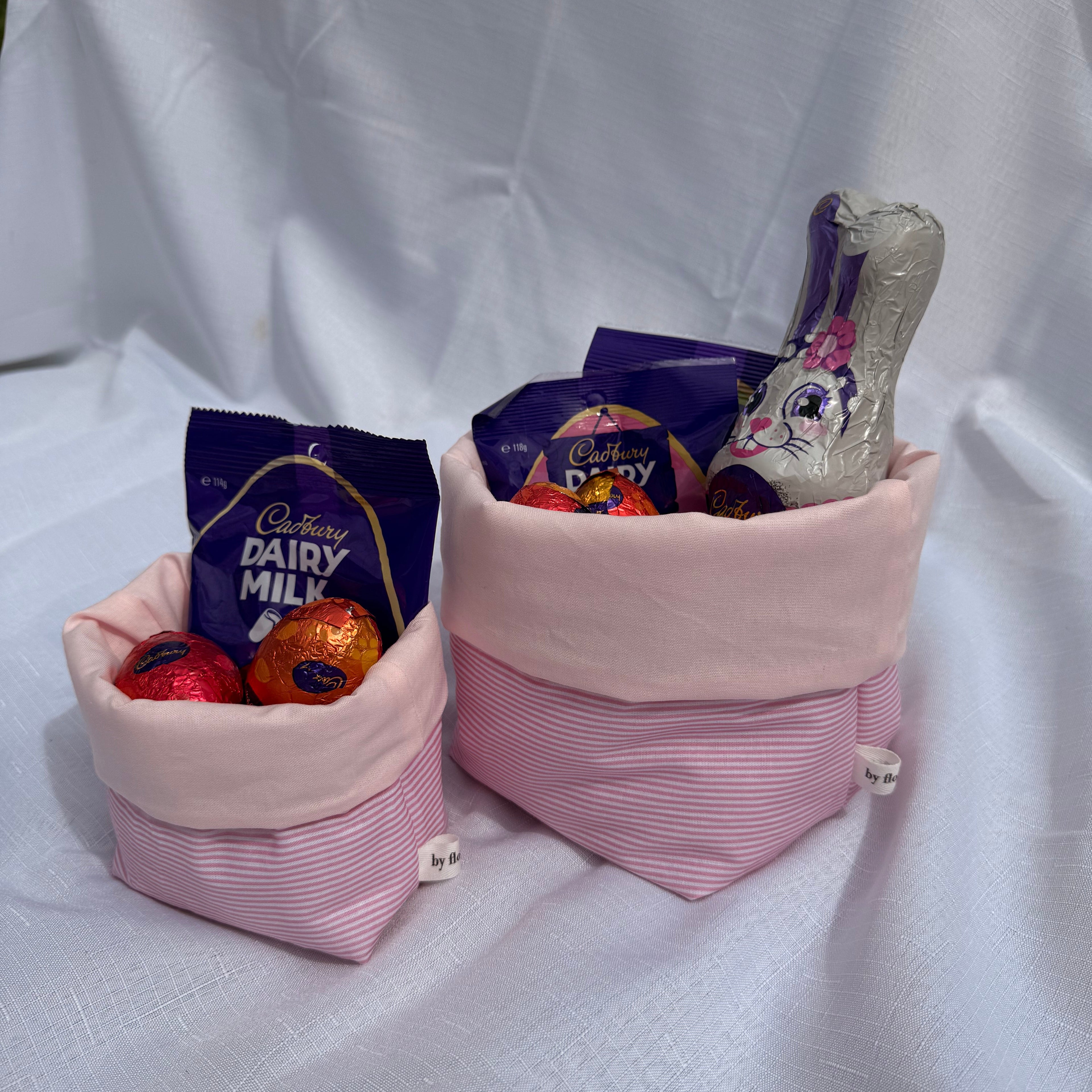 Pink fabric bags filled with Cadbury Dairy Milk chocolate bars on a white background